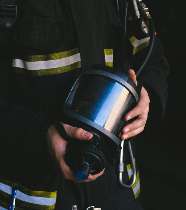 Close-up of a firefighter holding equipment with reflective stripes, showcasing safety gear.